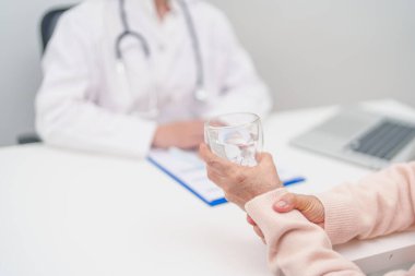 Hastanede bir bardak su içerken eli titreyen yaşlı bir kadın. Parkinson hastalığı Nisan farkındalık ayı, Karpal Tünel Sendromu, romatizma ve beyin hasarı ve nörolojik bozukluk konsepti 