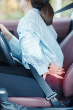Uzun süre araba kullanırken sırtı burkulmuş bir kadın. Piriforis Sendromu, bel ağrısı ve omurga sıkışması nedeniyle sırt ağrısı çekiyor. Ergonomik ve tıbbi konsept
