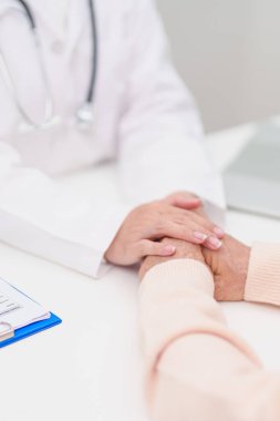 Doktor yaşlı kadın hastayla el ele tutuşuyor. Tıbbi konsültasyon sırasında empati ve destek gösteriyor. Güven, yaşlılar ve yaşlılar için sağlık, akıl sağlığı, danışmanlık ve duygusal danışmanlık 
