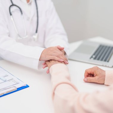 Doktor yaşlı kadın hastayla el ele tutuşuyor. Tıbbi konsültasyon sırasında empati ve destek gösteriyor. Güven, yaşlılar ve yaşlılar için sağlık, akıl sağlığı, danışmanlık ve duygusal danışmanlık 