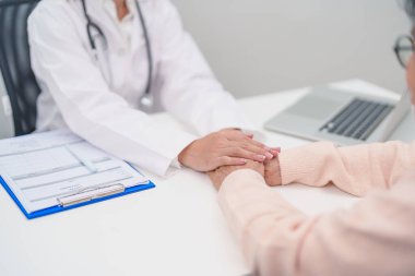 Doktor yaşlı kadın hastayla el ele tutuşuyor. Tıbbi konsültasyon sırasında empati ve destek gösteriyor. Güven, yaşlılar ve yaşlılar için sağlık, akıl sağlığı, danışmanlık ve duygusal danışmanlık 