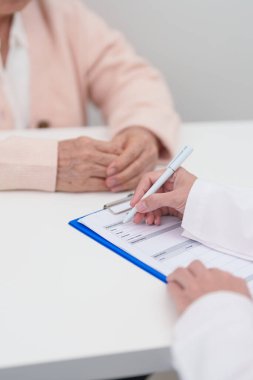 Hastanedeki doktora danışmanlık yapan kıdemli bir kadın. Yaşlı hasta konuşuyor ve hastalıkları paylaşıyor. Doktor dinler, soru sorar ve not alır. Tıbbi danışmanlık ve yaşlılık sağlığı konsepti 