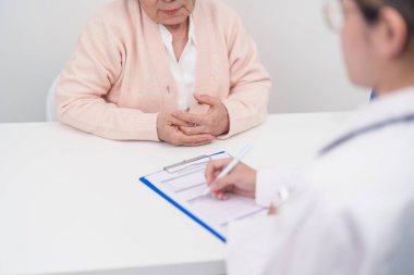 Hastanedeki doktora danışmanlık yapan kıdemli bir kadın. Yaşlı hasta konuşuyor ve hastalıkları paylaşıyor. Doktor dinler, soru sorar ve not alır. Tıbbi danışmanlık ve yaşlılık sağlığı konsepti 