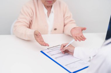 Hastanedeki doktora danışmanlık yapan kıdemli bir kadın. Yaşlı hasta konuşuyor ve hastalıkları paylaşıyor. Doktor dinler, soru sorar ve not alır. Tıbbi danışmanlık ve yaşlılık sağlığı konsepti 