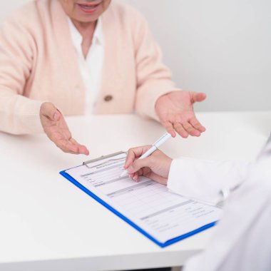 Hastanedeki doktora danışmanlık yapan kıdemli bir kadın. Yaşlı hasta konuşuyor ve hastalıkları paylaşıyor. Doktor dinler, soru sorar ve not alır. Tıbbi danışmanlık ve yaşlılık sağlığı konsepti 