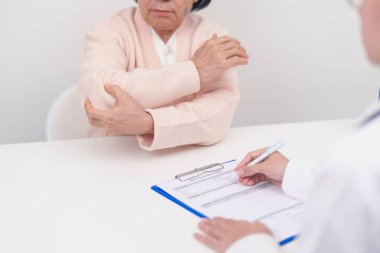 Dirsek ağrısı çeken ve hastanede danışmanlık yapan yaşlı bir kadın. Yan epikondil iltihabı ya da tenis dirseği yüzünden kas ağrısı. yaralanma, sağlık ve tıbbi danışma kavramı