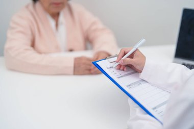Hastanedeki doktora danışmanlık yapan kıdemli bir kadın. Yaşlı hasta konuşuyor ve hastalıkları paylaşıyor. Doktor dinler, soru sorar ve not alır. Tıbbi danışmanlık ve yaşlılık sağlığı konsepti 