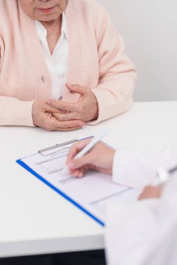 Hastanedeki doktora danışmanlık yapan kıdemli bir kadın. Yaşlı hasta konuşuyor ve hastalıkları paylaşıyor. Doktor dinler, soru sorar ve not alır. Tıbbi danışmanlık ve yaşlılık sağlığı konsepti 