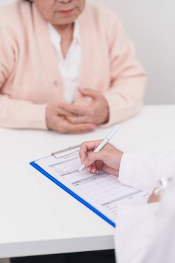 Hastanedeki doktora danışmanlık yapan kıdemli bir kadın. Yaşlı hasta konuşuyor ve hastalıkları paylaşıyor. Doktor dinler, soru sorar ve not alır. Tıbbi danışmanlık ve yaşlılık sağlığı konsepti 