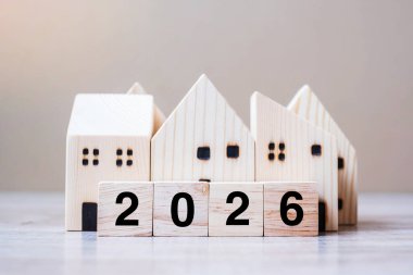 2026 Mutlu Yıllar, masa başı ahşap arka planda ev modeliyle. Bankacılık, gayrimenkul, yatırım, finans, tasarruf ve yeni yıl kararı kavramları