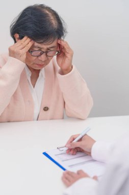 Kıdemli kadın baş ağrısı çekiyor ve bir hastalığa danışmanlık yapıyor. Yaşlı sağlık hastası, Tıbbi Teşhis, Migren, Beyin Tümörü, Beyin Felci, Bunama, Nörolojik Bozukluk, Alzheimer, Parkinson