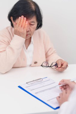 Yaşlı kadın hasta göz ağrısı çekiyor ve göz hastalıkları doktoruna danışıyor. Kıdemli Tıbbi Teşhis. Katarakt, glikoma, Yaşla İlgili Maküler Dejenerasyon, Diyabetik Retinopati, Vitreöz ve Sağlık 