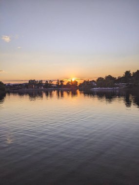 Köydeki gölün üzerinde gün batımı. Bir parktan görüntü, turuncu-mor tonda görüntü