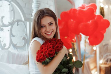 Bej rengi iç dairede bir buket kırmızı gülle romantik bir kadın. Şefkat ve kadının hisleri. Sevgililer Günü.