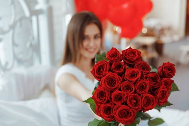 Bej rengi iç dairede bir buket kırmızı gülle romantik bir kadın. Şefkat ve kadının hisleri. Sevgililer Günü.