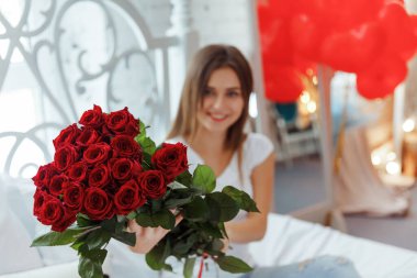 Bej rengi iç dairede bir buket kırmızı gülle romantik bir kadın. Şefkat ve kadının hisleri. Sevgililer Günü.