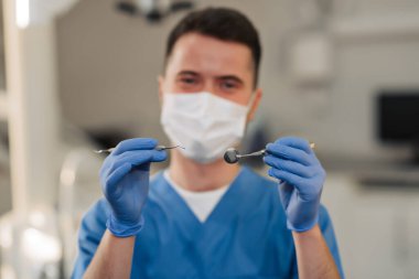 Genç erkek diş hekimi diş araçları elinde tutan.