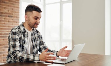 A happy young man works at a computer and communicates online.
