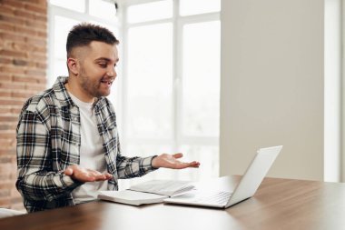 A happy young man works at a computer and communicates online.