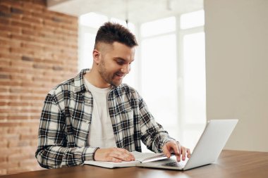A happy young man works at a computer and communicates online.