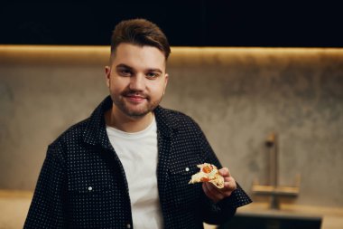 Handsome young man enjoying pizza in his kitchen. Unbelievably enjoys the taste.