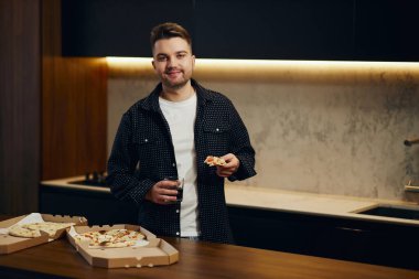 Handsome young man enjoying pizza in his kitchen. Unbelievably enjoys the taste.