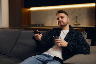 Büyük Tv programı. Uzaktan kumanda tutarak ve evde kanepede otururken Tv izlerken neşeli yakışıklı genç.