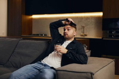 Büyük Tv programı. Uzaktan kumanda tutarak ve evde kanepede otururken Tv izlerken neşeli yakışıklı genç.
