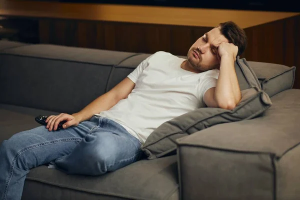 Beyaz tişörtlü genç bir adam, yorgun, TV karşısında uyuyakalmış. Tembel adam gece tek başına televizyon izliyor..