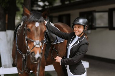 Kız binici at yarışlarına katılmak için atının eyer ayarlar.