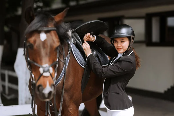 Stock image Girl rider adjusts saddle on her horse to take part in horse races.