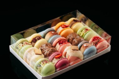 Gift set of large colored macaroons with different fillings and decorations, on a black isolated background. Confectionery concept.