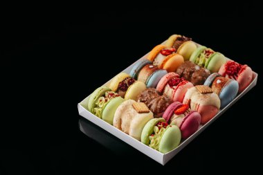 Gift set of large colored macaroons with different fillings and decorations, on a black isolated background. Confectionery concept.