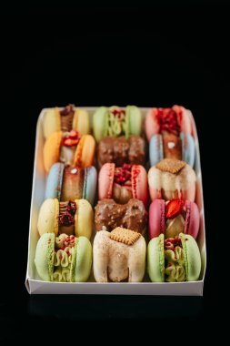 Gift set of large colored macaroons with different fillings and decorations, on a black isolated background. Confectionery concept.