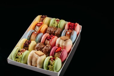 Gift set of large colored macaroons with different fillings and decorations, on a black isolated background. Confectionery concept.