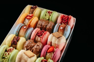 Gift set of large colored macaroons with different fillings and decorations, on a black isolated background. Confectionery concept.