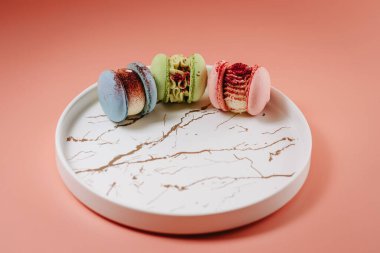 Colored large macaroons on a black plate, with various fillings. On a pink background.