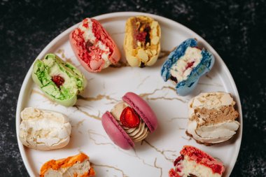 Many big bitten macaroons on a beautiful white plate, on a black isolated background. Photo for content.