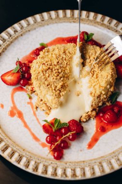 Baked Camembert in nut breading with berry sauce, decorated with strawberries. Restaurant serving of dishes. The girl cuts the camembert, the cheese oozes out and stretches.