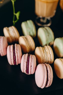 Macaroons of different colors on a black table. Confectionery concept.