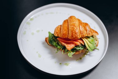 Beyaz tabakta tuzlanmış somon ve avokado dilimli kruvasan. Sağlıklı kahvaltı konsepti..