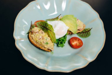 Tartare with tuna on crusty bread, with a poached egg, garnished with avocado and greens.