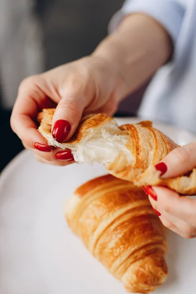 A girl with a red manicure tears a French croissant. The layers are torn apart.