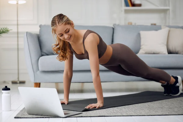 Fit young woman wearing sportswear working out at home doing planking exercise on carpet