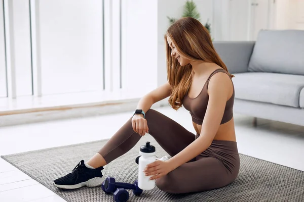 Young beautiful athletic girl in leggings and top does stretching exercises. Healthy lifestyle. A woman using smart watch and goes in for sports at home