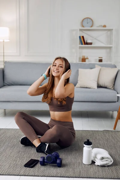 Portrait of a pretty cute sport girl heaving a break listening to music on her headphones while fitness training in a brown sport suit