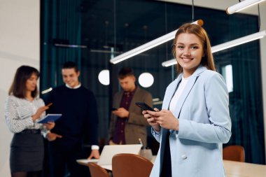 Happy office worker looks at camera while holding the phone.