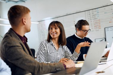 Office worker works with papers while two other workers talk.
