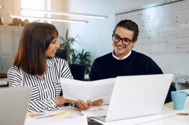Duo of the office workers are smiling at each other.