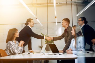 Duo of the office workers happily shake their hands after successful deal.